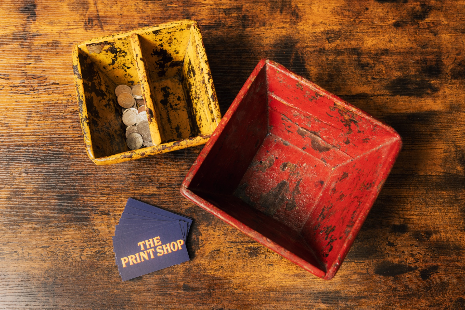 Vintage red and yellow shop tins beside printed cards on a wood bench